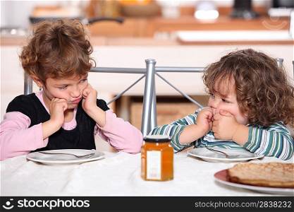Grumpy children at a table with pancakes