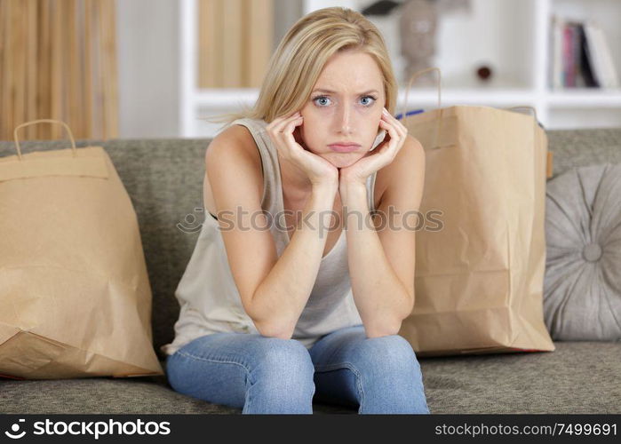 grumpy woman sat on sofa with shopping bags around her