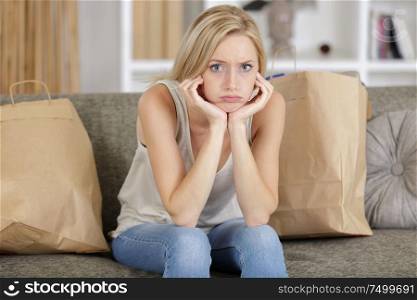 grumpy woman sat on sofa with shopping bags around her