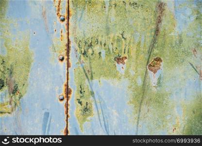 Grunge background: old rusty metal surface covered with blue and green paint flaking and cracking texture, with seam and rivets