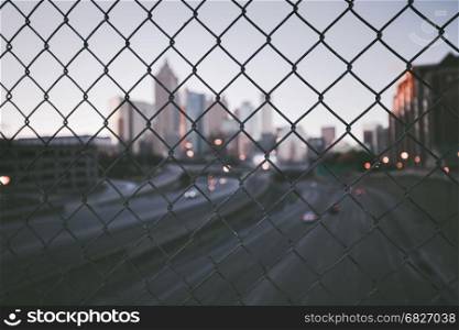 Grunge city skyline through the wire mesh fence. Abstract blurred cityscape background