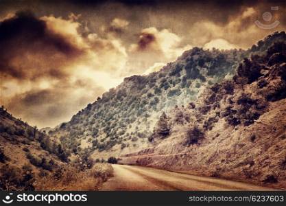Grunge style photo of road passing between mountains, dramatic sunset cloudscape, beautiful landscape, overcast weather&#xA;