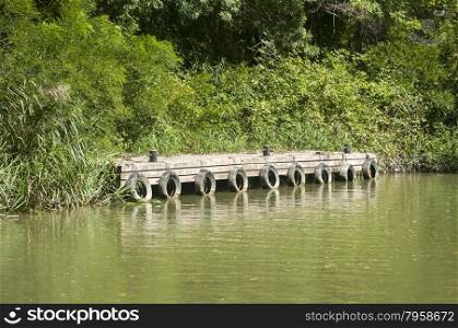 Grunge wooden river pier for fishing boats with used tires as bumpers