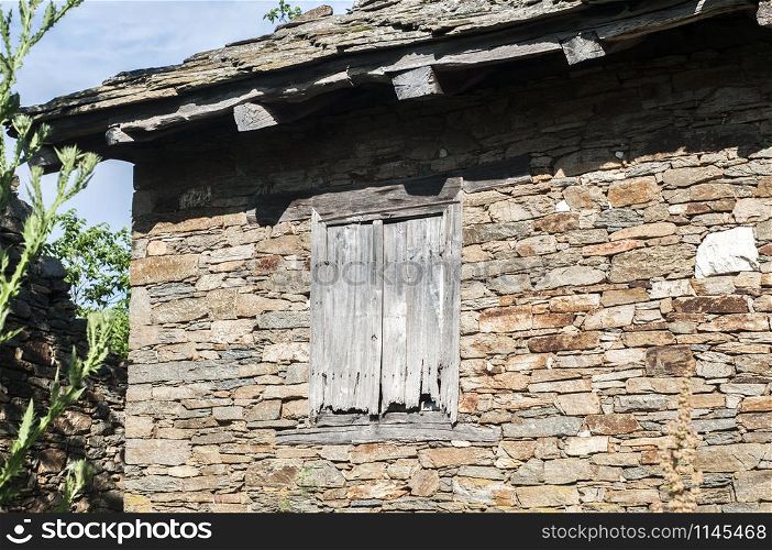Grunge wooden window on abandoned rural house stone wall closeup