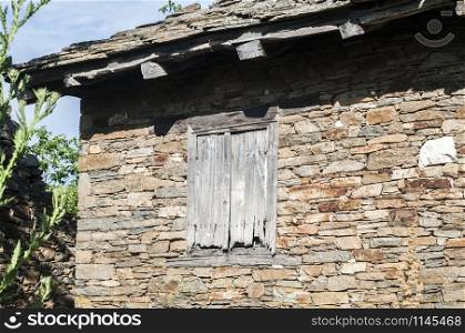 Grunge wooden window on abandoned rural house stone wall closeup