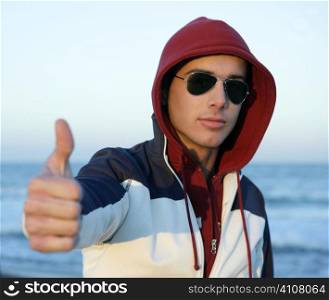 Grunge young man with hood and sunglasses at the beach