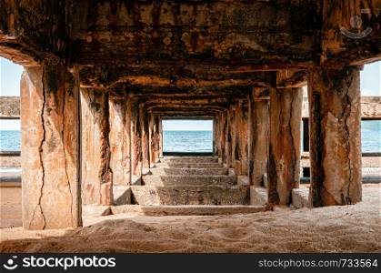 Grungy dirty rustic concrete pillar under old ship port pier bridge on sand beach