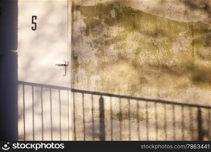 grungy wall and door with number 5 of deserted parking garage plus shadow of railing