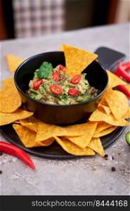 Guacamole dip with tortilla chips or nachos on black serving board.. Guacamole dip with tortilla chips or nachos on black serving board