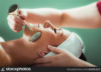 Guasha face massage in beauty salon, massage technique for stimulating pressure points on the face, using jade stone roller