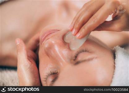 Guasha face massage with jade stone. Close-up of a young woman’s face. Guasha Jade Face Sculpting Massage 