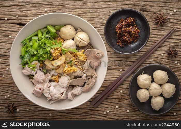 Guay Teaw, Guay Teow, Guay Tiew, Kuay Teow Neua, Thai food, noodle soup with beef, meatball, crackling, fried garlic, morning glory, chili, herb, pepper on rustic wood texture background, top view