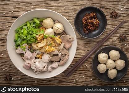 Guay Teaw, Guay Teow, Guay Tiew, Kuay Teow Neua, Thai food, noodle soup with beef, meatball, crackling, fried garlic, morning glory, chili, herb, pepper on rustic wood texture background, top view