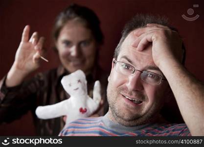 Guilty man with upset woman poking voodoo doll in the background