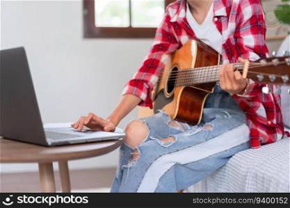 Guitar and singer concept, Young asian woman playing acoustic guitar while learning music on laptop.