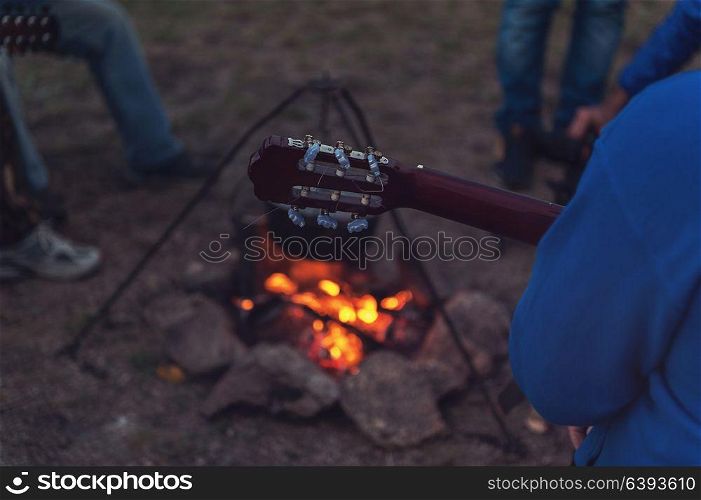 guitar near the campfire. Closeup photo of the man playing o guitar near the campfire