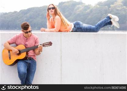 Guitarist and his muse. . Love romance music talent passion dating concept. Guitarist and his muse. Young man playing guitar with girl lying on wall with scenery background.