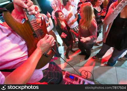 Guitarist maxing out on his guitar with a large group of people on the dance floor in a nightclub