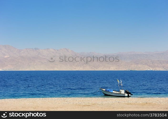 Gulf of Eilat Red Sea, the boat on the shore and Jordanian mountains in the background.