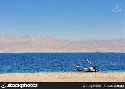 Gulf of Eilat Red Sea, the boat on the shore and Jordanian mountains in the background.