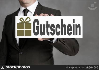 Gutschein (in german Gift card) is held by a businessman.. Gutschein (in german Gift card) is held by a businessman