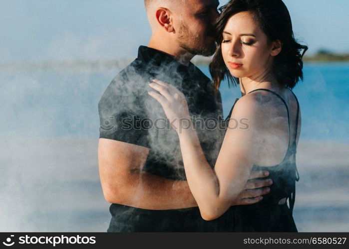 guy and a girl in black clothes hug inside a white smoke