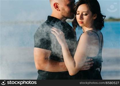 guy and a girl in black clothes hug inside a white smoke