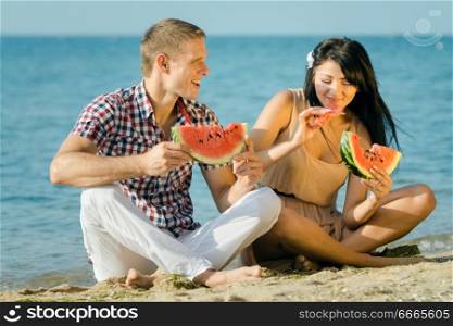 guy and a girl on the seashore eating a ripe red watermelon