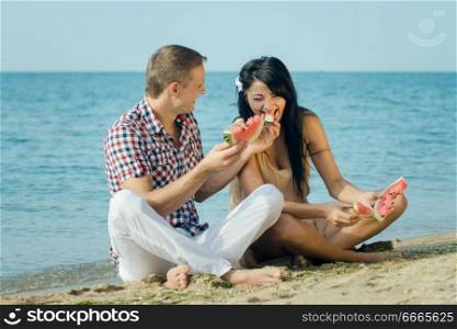 guy and a girl on the seashore eating a ripe red watermelon
