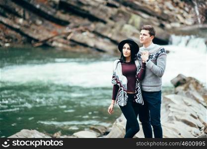 guy and girl in warm sweaters walking along a mountain river, love story