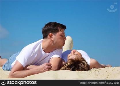 guy blows on lying near to it on sand girl
