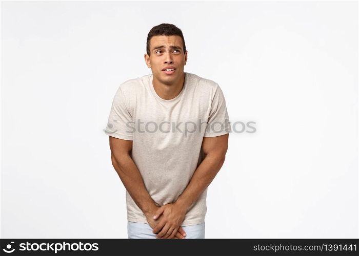 Guy cant hold anymore, need go toilet, looking at clock upper right corner, bending and touching groin area as have to pee, standing white background uncomfortable and impatient. Copy space. Guy cant hold anymore, need go toilet, looking at clock upper right corner, bending and touching groin area as have to pee, standing white background uncomfortable and impatient