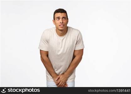 Guy cant hold anymore, need go toilet, looking at clock upper right corner, bending and touching groin area as have to pee, standing white background uncomfortable and impatient. Copy space. Guy cant hold anymore, need go toilet, looking at clock upper right corner, bending and touching groin area as have to pee, standing white background uncomfortable and impatient