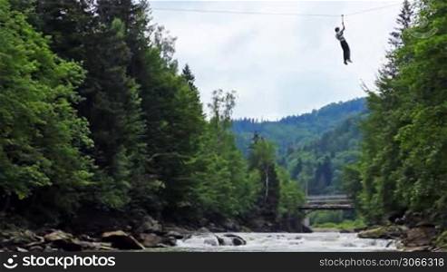 guy hanging on rope slowly moves over mountain river