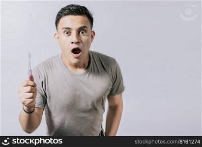 Guy holding toothbrush with amazed face isolated on white, Surprised young man holding a toothbrush. Amazed teenager holding toothbrush isolated