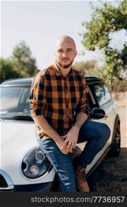 Guy in a plaid shirt next to a white car in nature