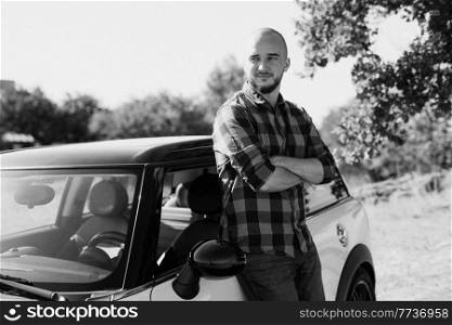 Guy in a plaid shirt next to a white car in nature