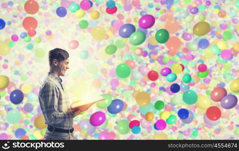 Guy in casual read book. Young man student with book in hands among colorful balloons