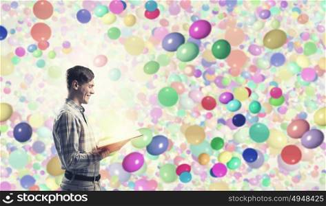 Guy in casual read book. Young man student with book in hands among colorful balloons