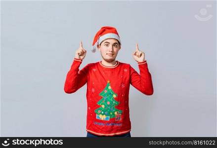 Guy in Christmas clothes pointing and recommending. Portrait of guy in sweater and christmas hat pointing up isolated. Caucasian young man in Christmas clothes pointing up an advertisement