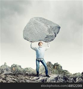 Guy lifting stone. Young strong man holding huge stone above head