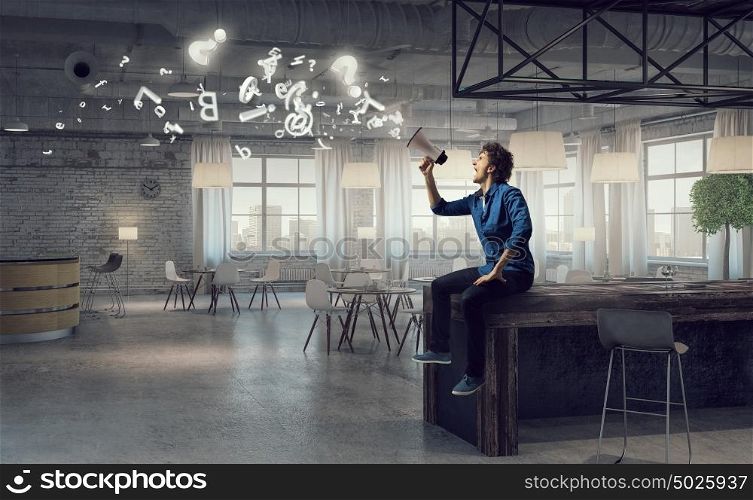 Guy making announcement. Emotional man screaming in megaphone while sitting on table in office
