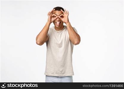 Guy popping eyes and looking amused through finger glasses. Happy carefree handsome man in t-shirt, showing goggles stick tongue funny, standing amazed and astonished white background.. Guy popping eyes and looking amused through finger glasses. Happy carefree handsome man in t-shirt, showing goggles stick tongue funny, standing amazed and astonished white background