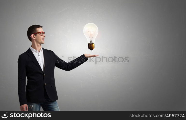 Guy presenting bright idea. Young student guy in jacket showing light bulb in palm