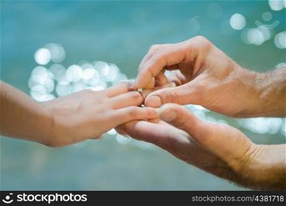 guy&rsquo;s hand puts an wedding ring on a girl&rsquo;s hand