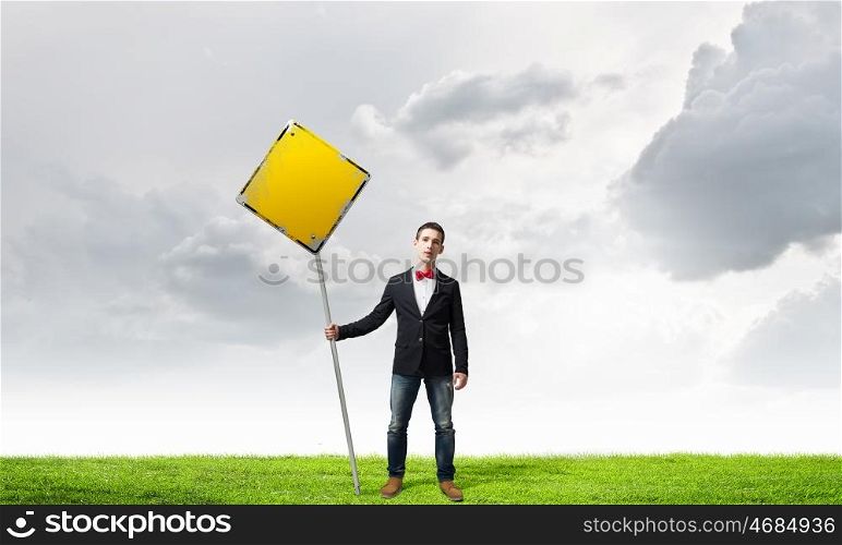 Guy showing roadsign. Young man in jacket and bowtie holding yellow sign