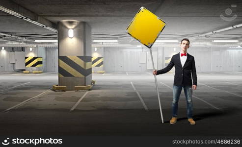 Guy showing roadsign. Young man in jacket and bowtie on parking holding sign