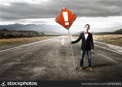 Guy showing roadsign. Young man in jacket and bowtie on road holding sign