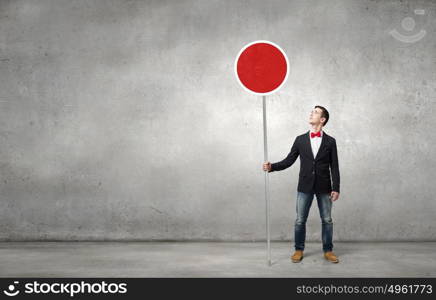 Guy showing roadsign. Young man in jacket and bowtie on road holding sign