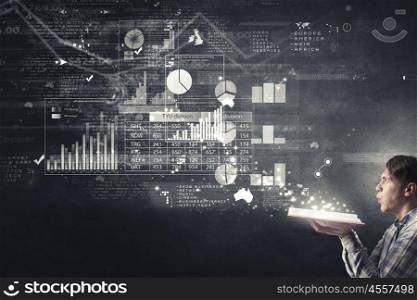 Guy studying finances. Young man with opened book in hands and infographs on wall blowing on pages